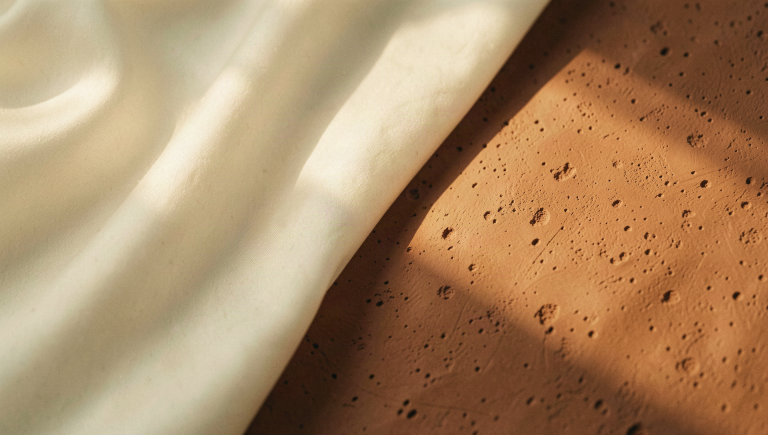 'Two contrasting tactile surfaces meeting along a soft diagonal - smooth ivory silk and freckled terracotta clay'